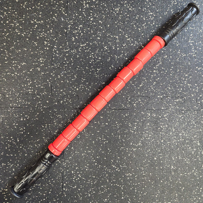 The Reflex Flexible Massage Stick positioned on a gym floor, with a clear view of its flexible design and black-and-red color scheme.